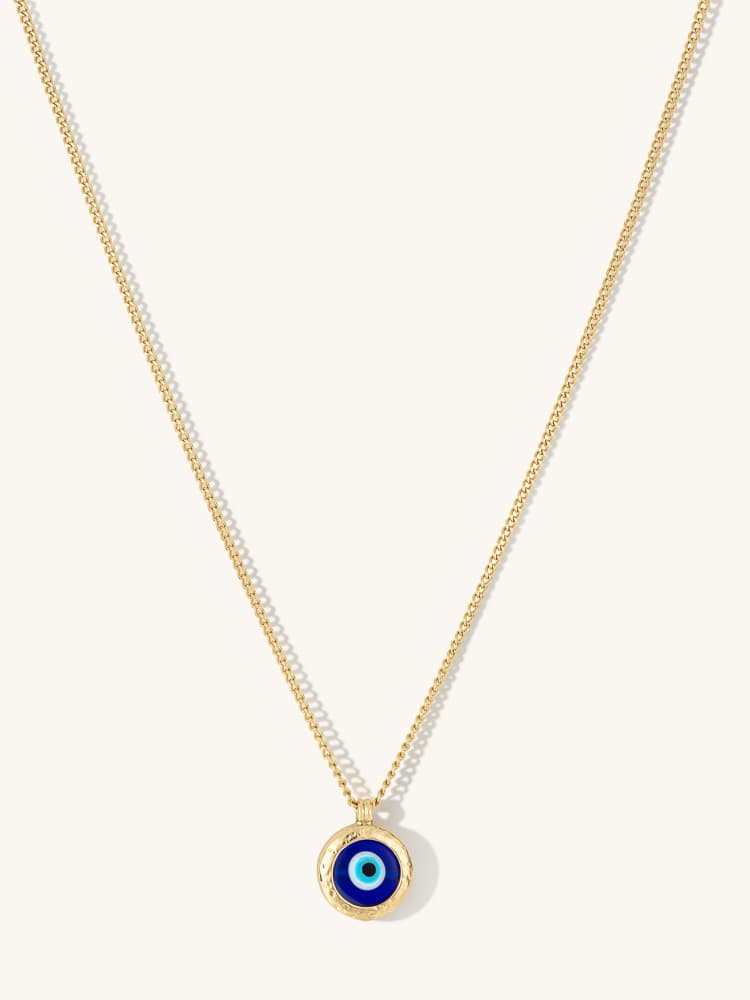 Gold necklace with a blue eye pendant photographed on a pale background