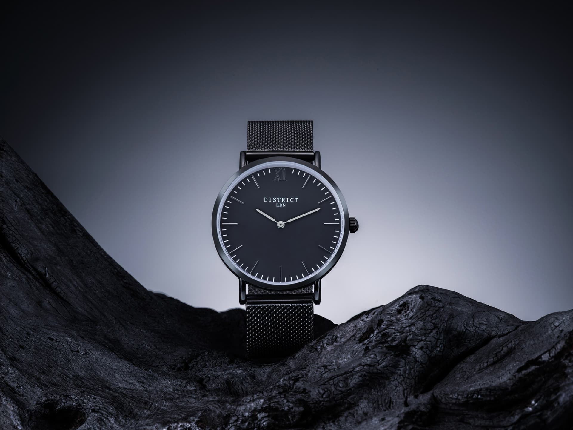 Black mesh watch on textured stone, with controlled lighting defining its face and strap